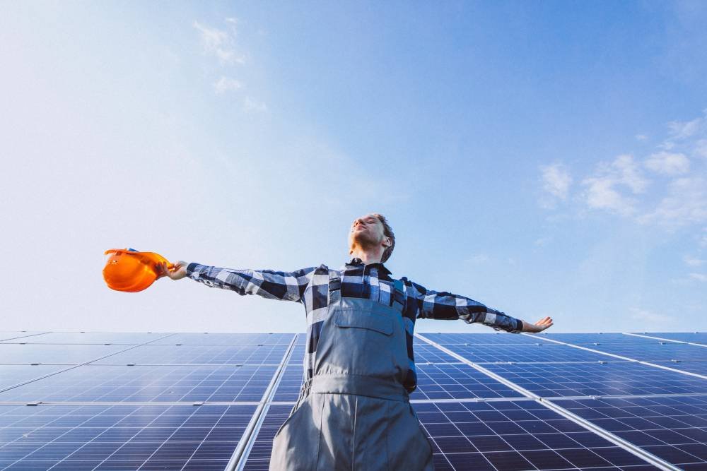 Foto de un hombre feliz delante de placas solares fotovoltaicas para autoconsumo